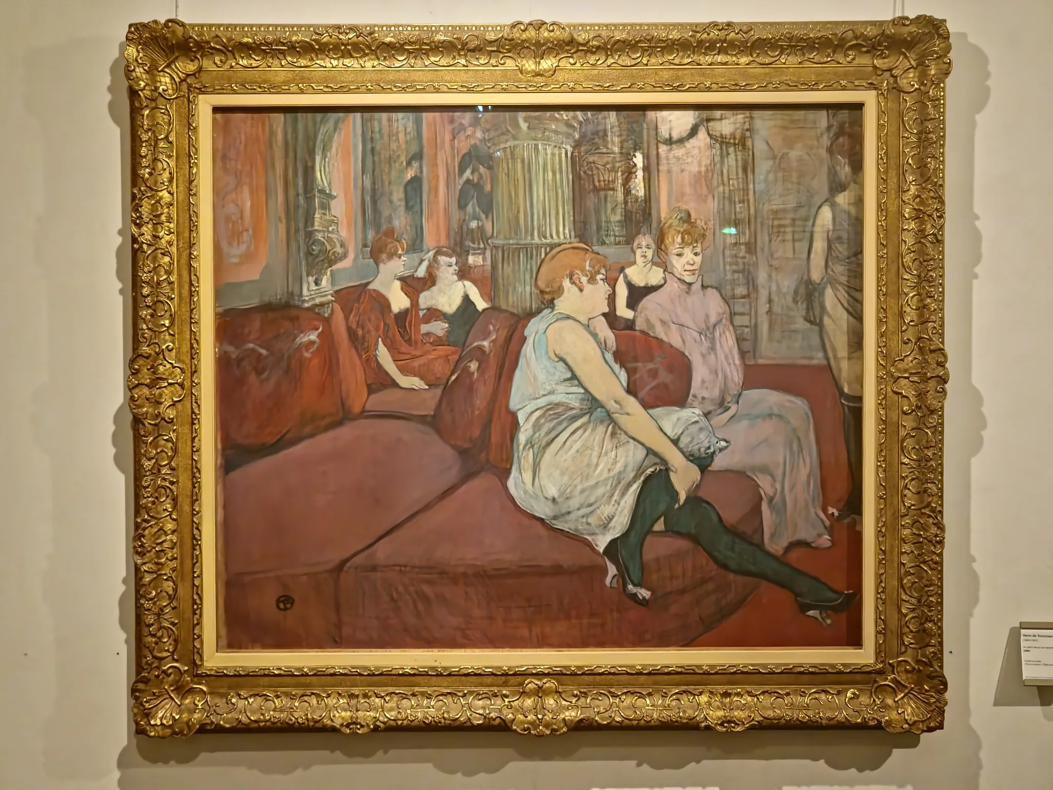 Scène d’intérieur au salon de la rue des Moulins peinte par Henri de Toulouse-Lautrec en 1894, femmes assises sur des banquettes rouges dans une maison close parisienne.