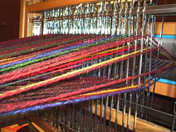 Vue arrière d’un métier à quatre cadres : fils de chaîne colorés traversant les lisses