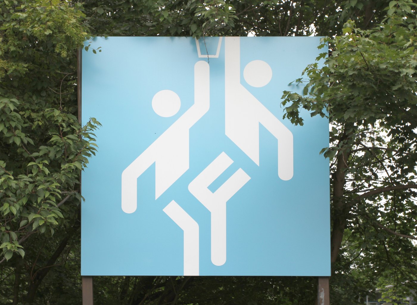 Pictogramme blanc de basket-ball de Munich 1972 photographié sur un panneau bleu clair entouré d’arbres