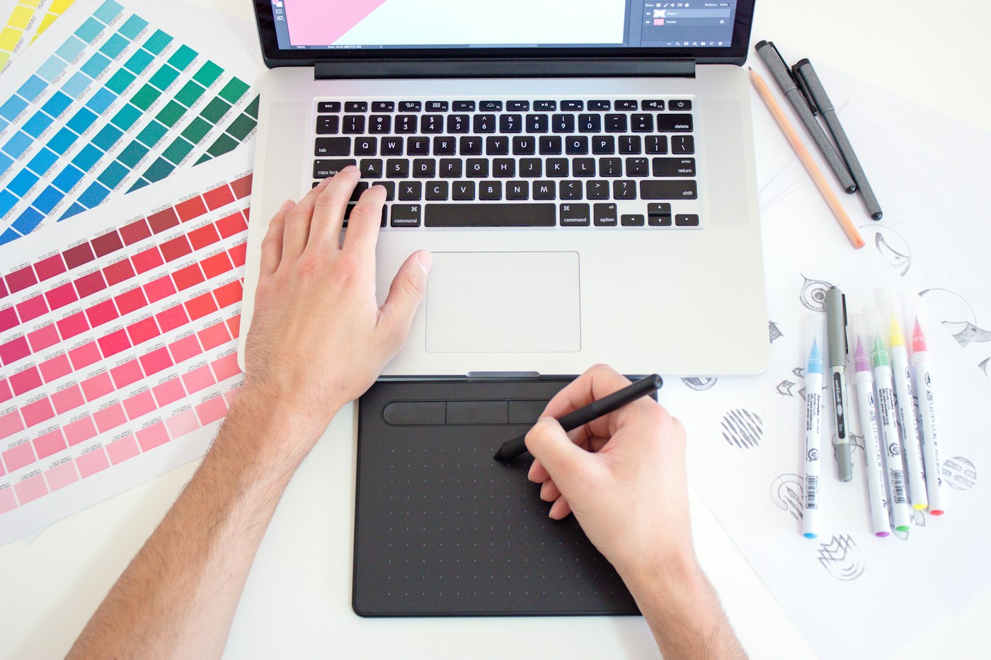Travail graphique associant ordinateur, nuanciers et gestes de sélection sur une table.